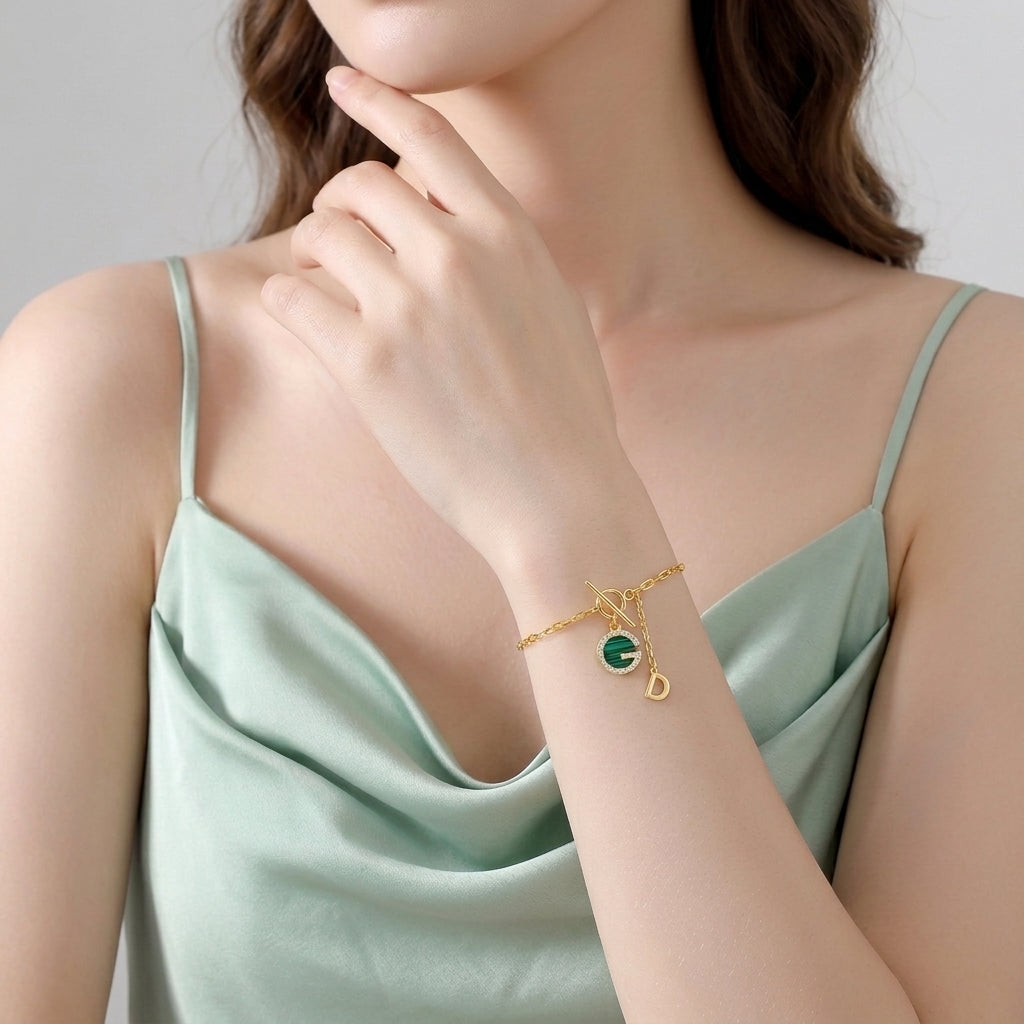 Une femme qui porte une robe verte et porte le Bracelet Malachite – Lumière Sylvestre en argent plaqué or, orné d'un pendentif rond en malachite et d'une breloque lettre D.