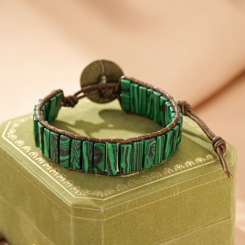 Bracelet en Malachite avec des perles rectangulaires vertes et noires, monté sur un cordon en cuir marron et fermé par un bouton en bronze.