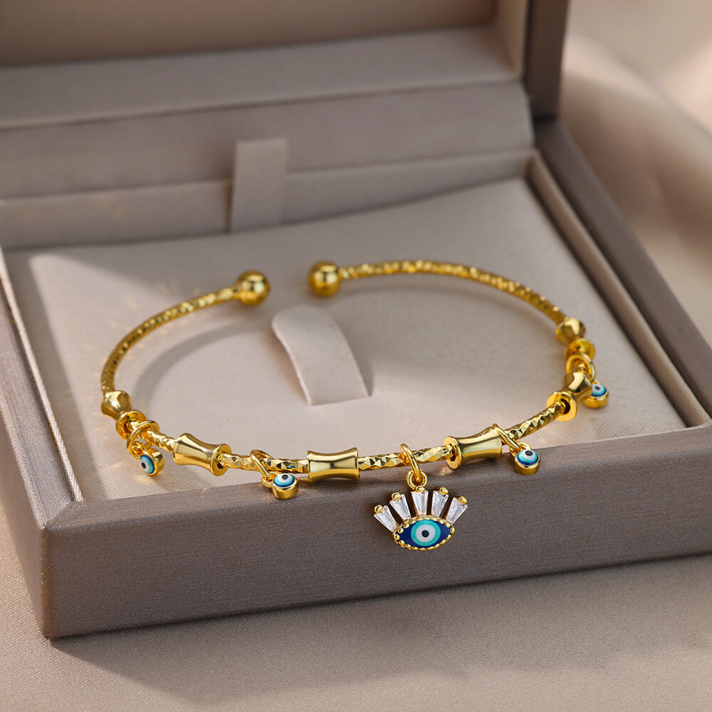 Bracelet jonc doré style bohème avec breloques œil bleu et zircon blanc, orné de perles et de motifs bambou.