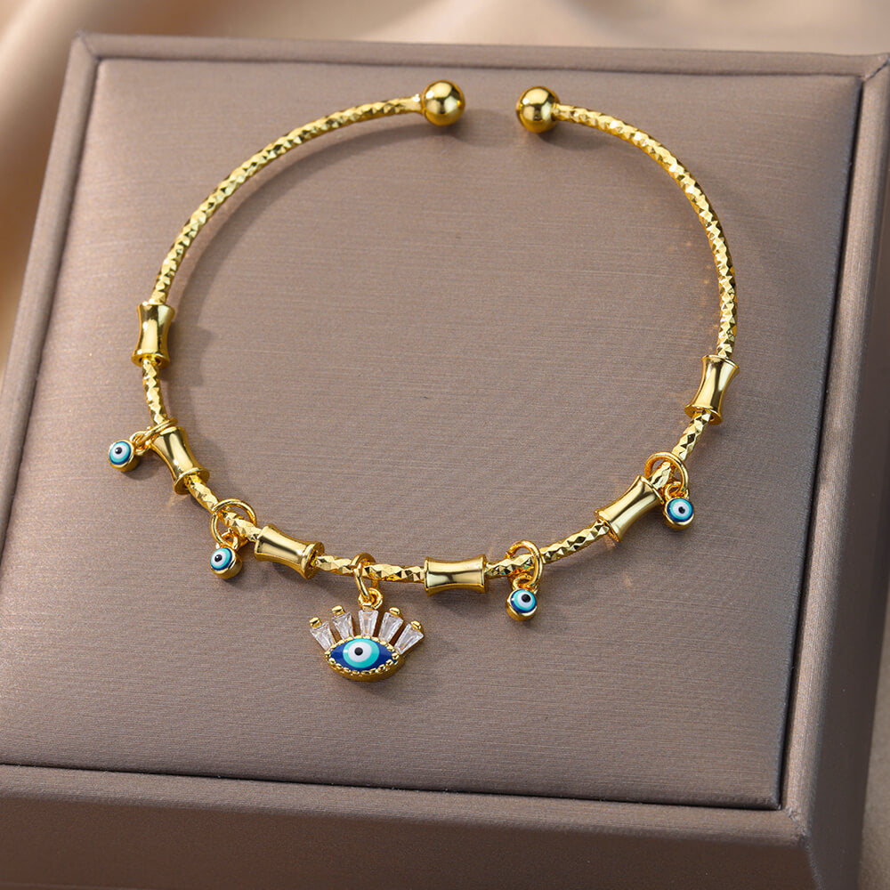 Bracelet jonc ouvert doré orné de plusieurs petits pendentifs œil bleu et d'un pendentif œil stylisé en zircon au centre, avec des éléments décoratifs en forme de bambou.