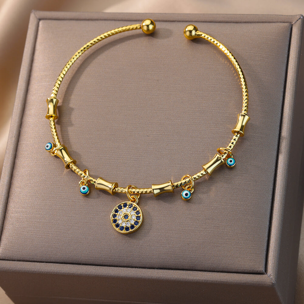 Bracelet jonc doré avec breloques œil bleu et un pendentif central œil bleu serti de zircons blancs et bleus.