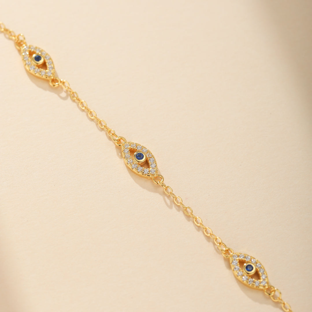 Bracelet plaqué or avec trois pendentifs œil bleu sertis de zircons blancs brillants, symbolisant la protection contre le mauvais œil.