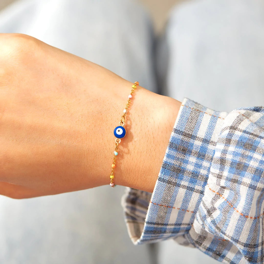 Bracelet fin en argent 925 avec un œil bleu au centre et de petites perles colorées sur le fil, porté au poignet.