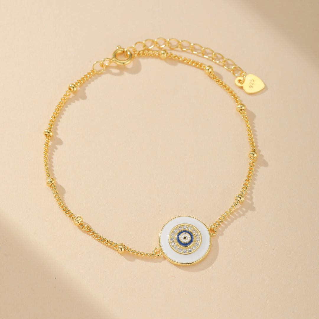 Bracelet fin en argent 925 plaqué or avec un pendentif rond blanc orné d'un œil bleu et de zircons brillants, orné de petites perles tout le long de la chaîne.