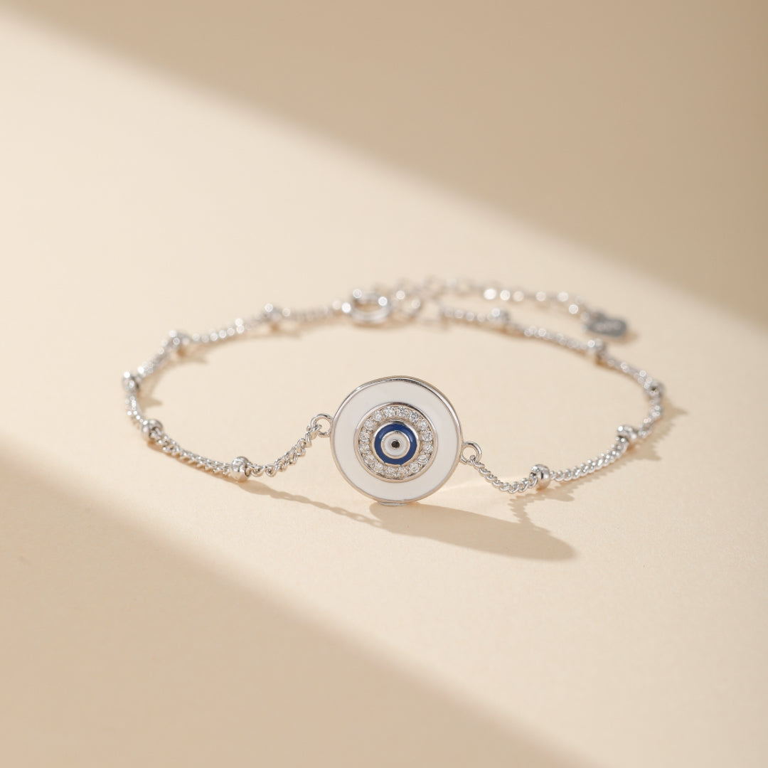 Bracelet œil de protection en argent 925 avec un pendentif rond blanc orné d'un œil bleu et de zircons.