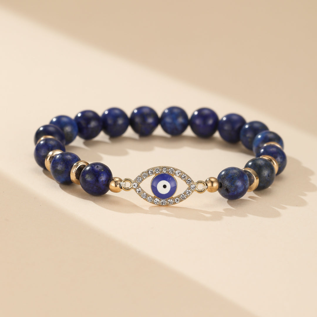 Bracelet élastique bleu lapis lazuli avec un pendentif œil bleu entouré de strass et des perles dorées.