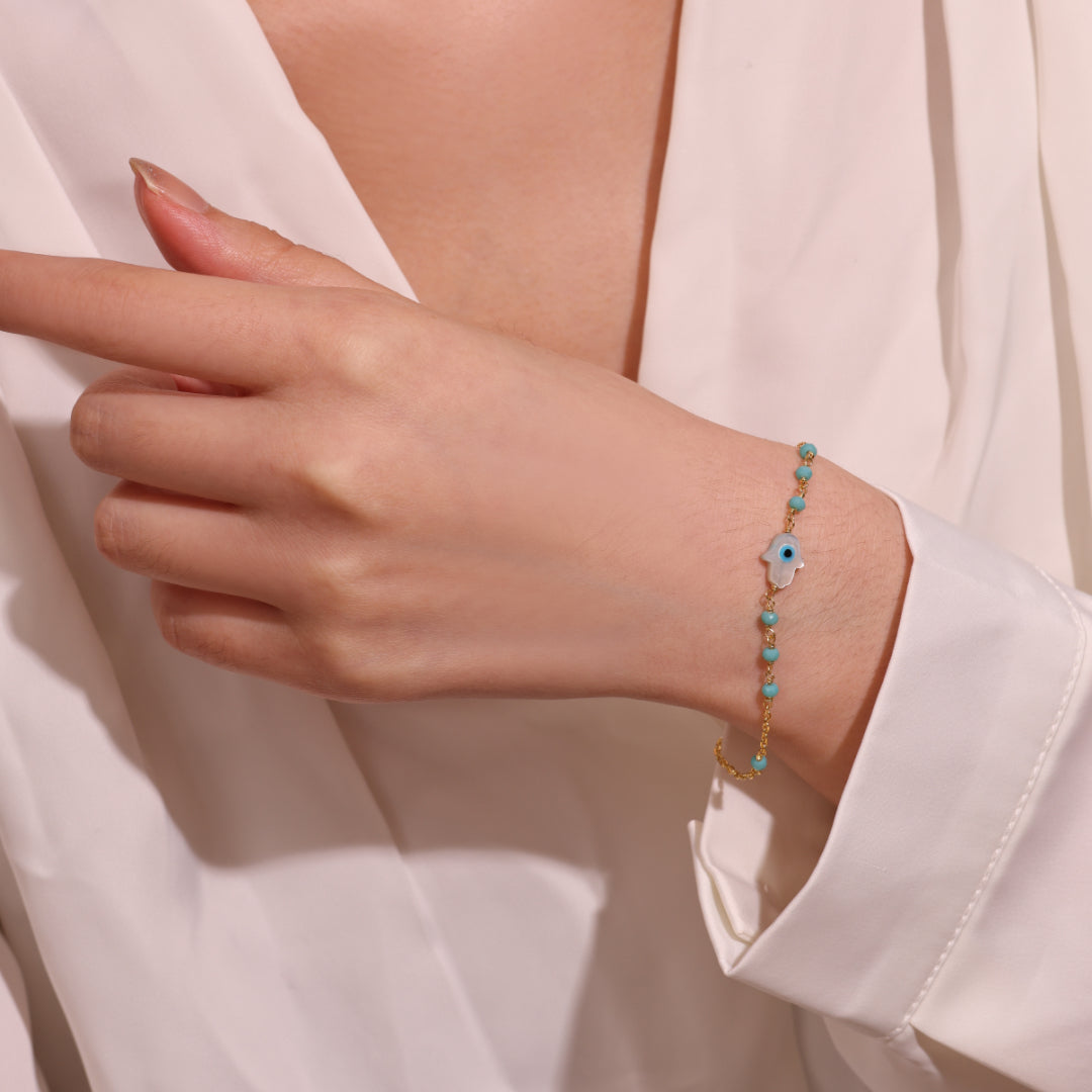 Bracelet fin en argent plaqué or orné d'une main de Fatma ornée d'un œil bleu et de petites pierres turquoises bleues.