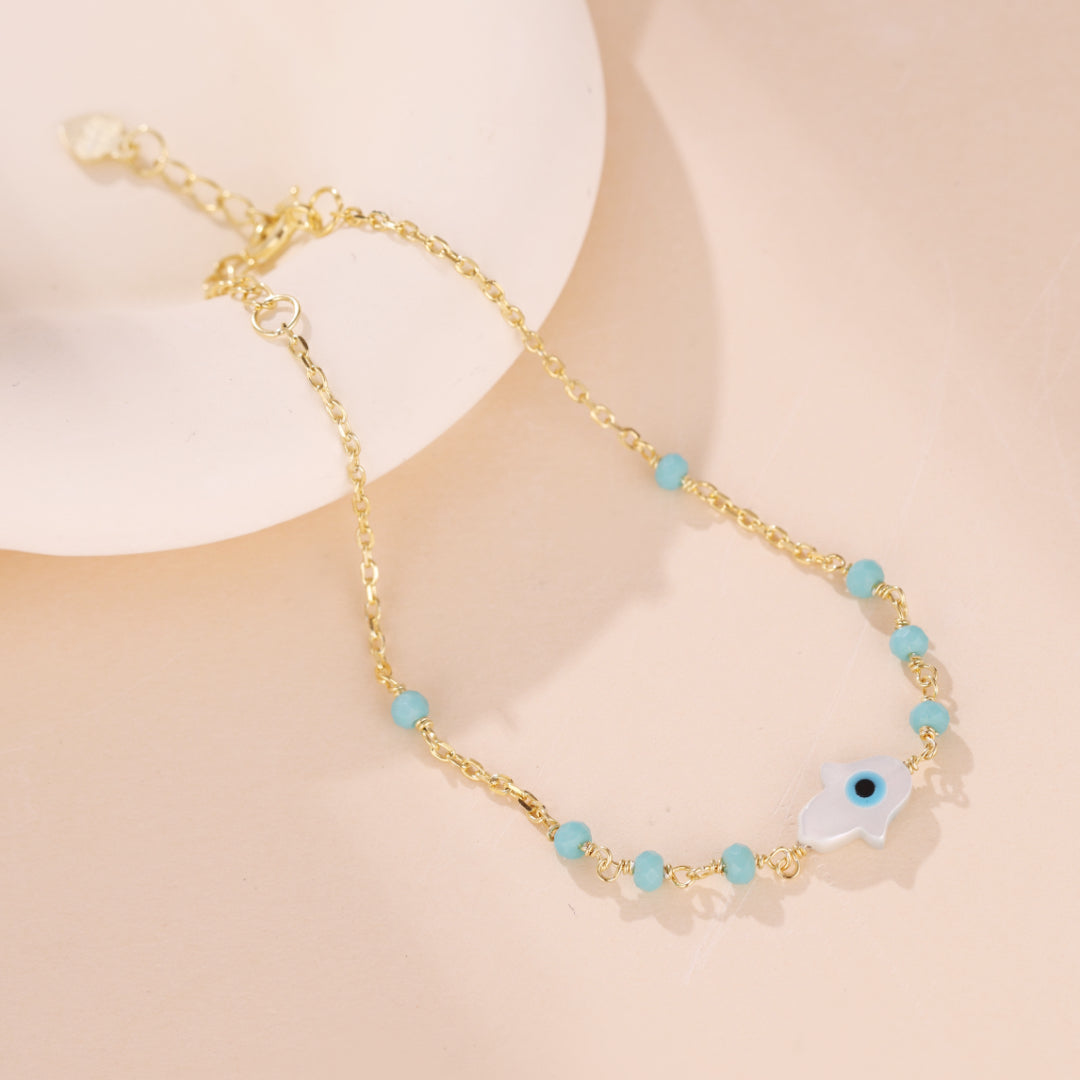 Bracelet fin en argent plaqué or avec une chaîne délicate ornée de petites perles turquoise et un pendentif main de Fatma avec un œil bleu au centre.