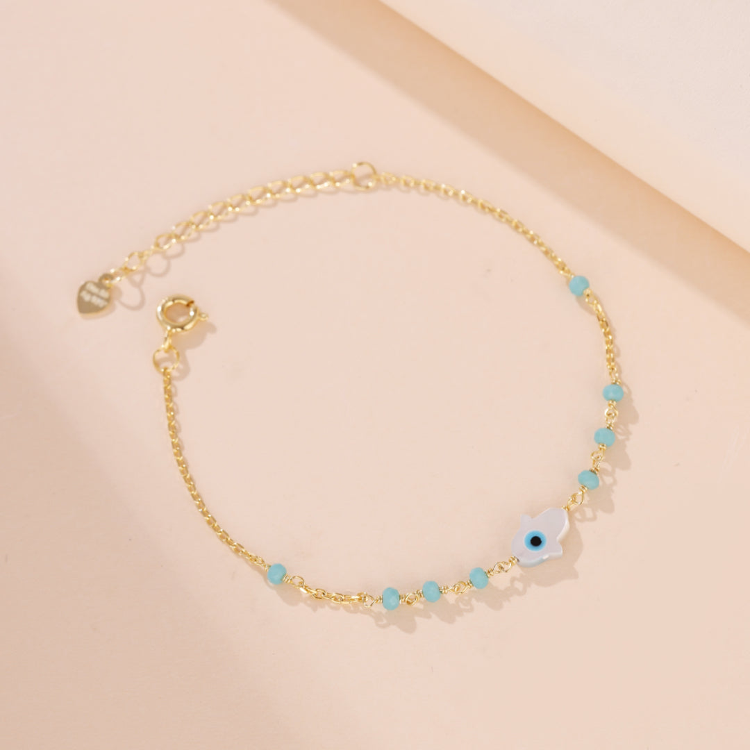 Bracelet chaîne fine en argent plaqué or orné de petites perles bleues et d'un pendentif main de Fatma œil bleu au centre, symbolisant la protection.