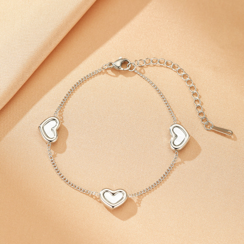 Bracelet fin en argent avec quatre cœurs nacrés blancs disposés le long de la chaîne, fermoir mousqueton et chaîne d'extension.