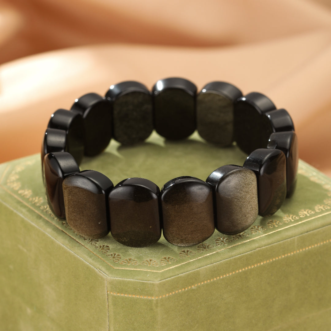 Bracelet en obsidienne dorée aux reflets cuivrés, monté sur un écrin vert.
