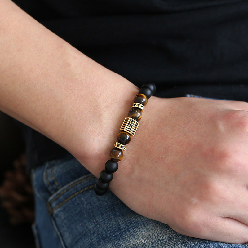 Bracelet homme en onyx noir mat et œil de tigre avec un élément central cubique doré incrusté de zircons, porté au poignet.