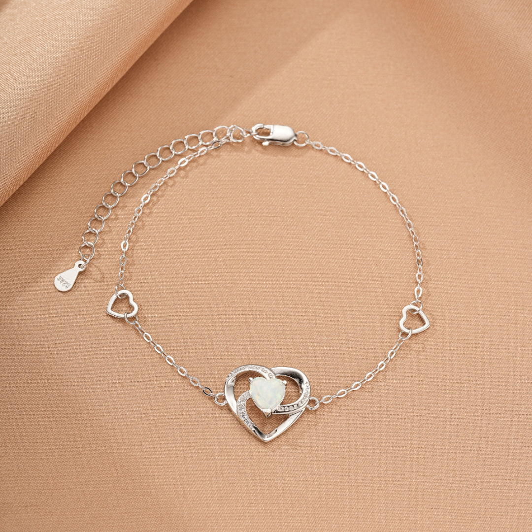 Bracelet en argent avec un pendentif en forme de cœur orné d'une opale centrale et de petits cœurs tout au long de la chaîne.