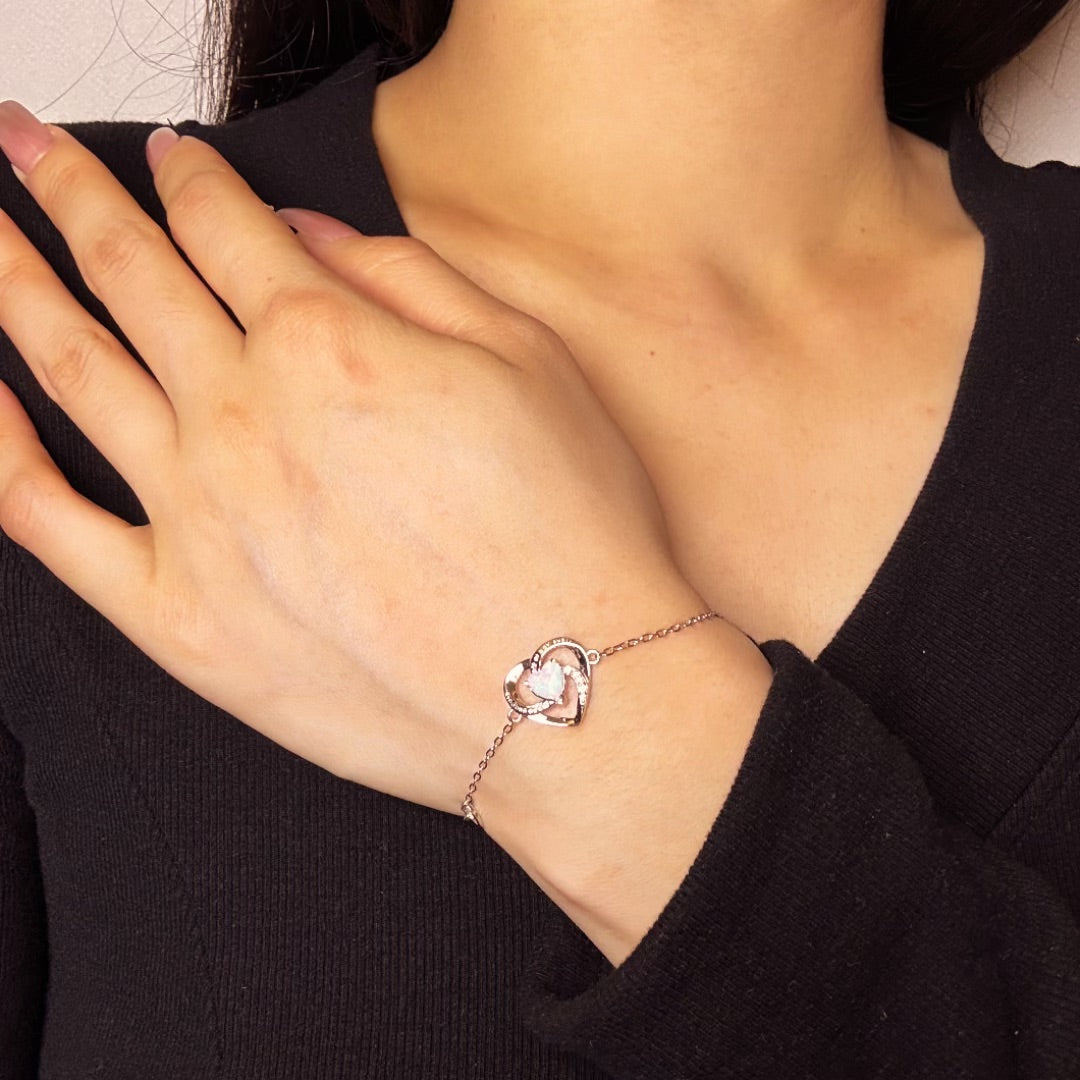Bracelet en argent avec un pendentif en forme de cœur orné d'une opale blanche et de zirconiums scintillants, porté au poignet d'une femme.