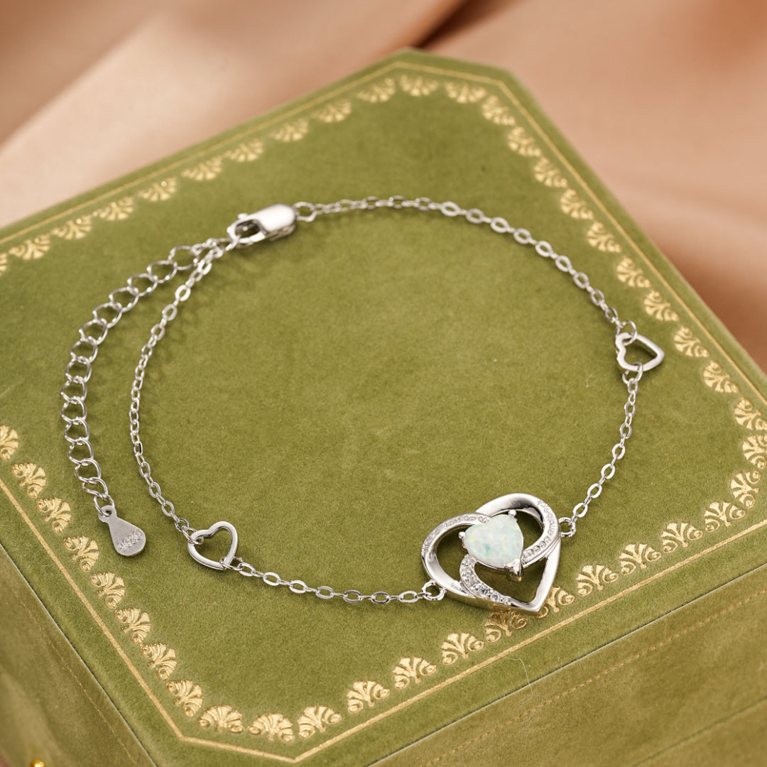 Bracelet en argent avec un pendentif en forme de cœur orné d'une opale et de petits cristaux, et de cœurs secondaires sur la chaîne.