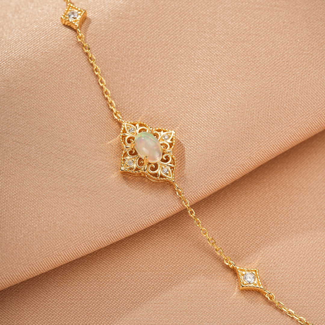 Gros plan d'un bracelet en plaqué or 10 carats avec une opale ovale centrale sertie dans un motif ajouré complexe, orné de petits diamants et d'un motif en losange sur la chaîne.
