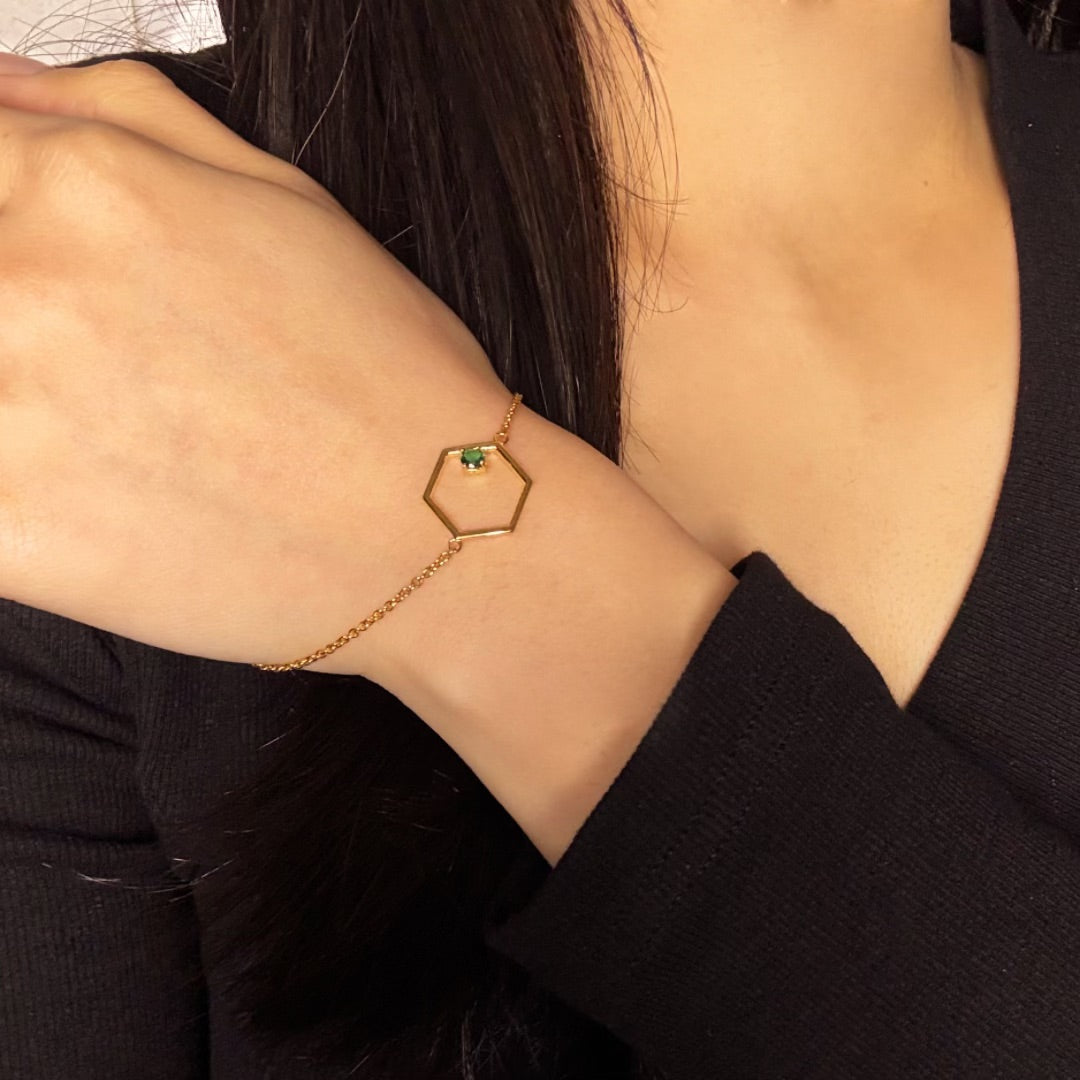 Bracelet fin en argent plaqué or avec un pendentif hexagone orné d'une petite pierre verte, porté au poignet d'une femme.