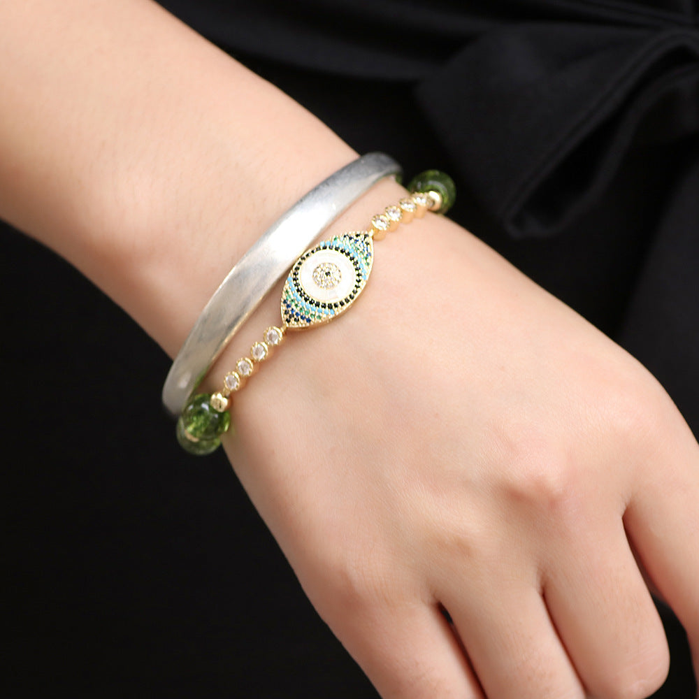 Bracelet en péridot avec un pendentif œil bleu et blanc serti de zircons et de perles, porté au poignet d'une femme.