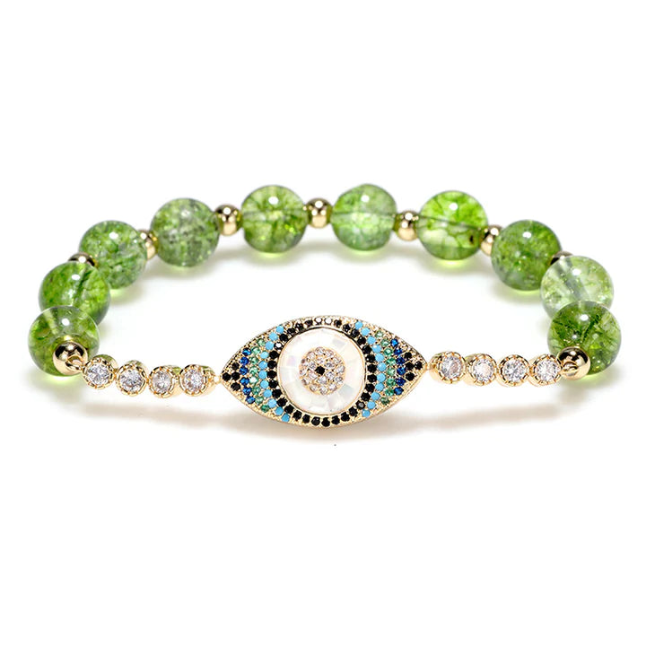 Bracelet "Abondance" orné d'un œil du mal bleu et blanc serti de cristaux, enfilé sur des perles rondes vertes de péridot et de petites perles dorées.