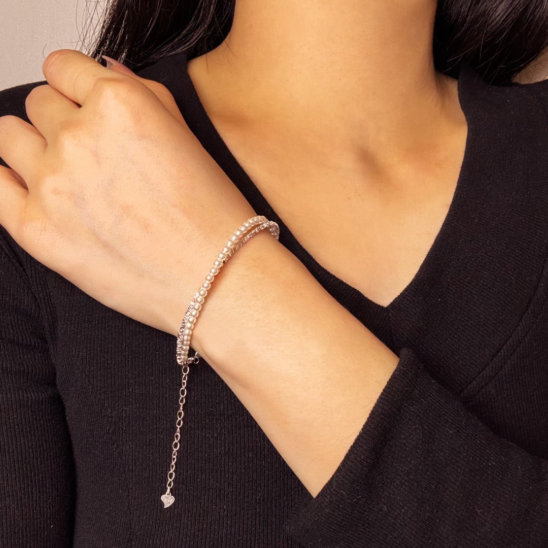 Bracelet en argent avec double rangée de petites perles et pendentif en forme de cœur, porté au poignet d'une femme.