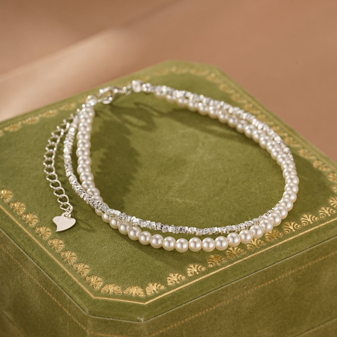 Bracelet double rang avec perles nacrées et chaînette en argent, orné d'un petit pendentif cœur.