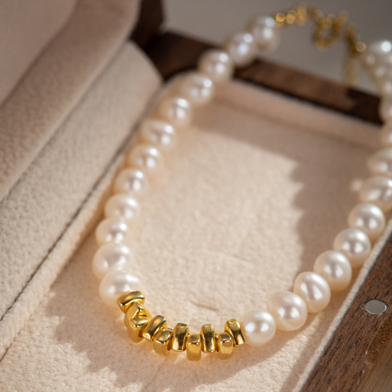 Bracelet en perles blanches avec accents dorés texturés, monté sur une monture en argent plaqué or, présenté dans une boîte