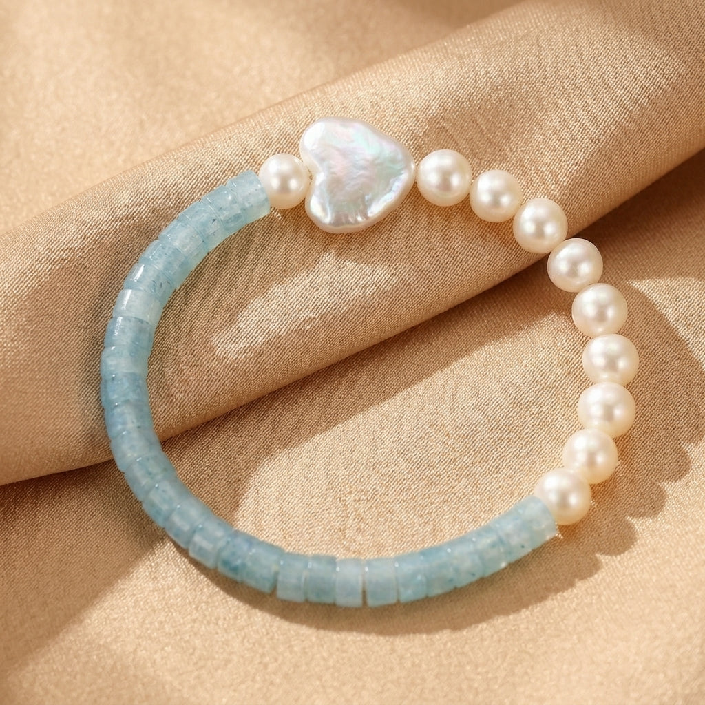 Bracelet en aigue-marine et perles d'eau douce avec un pendentif en forme de cœur en nacre, sur un fond texturé.