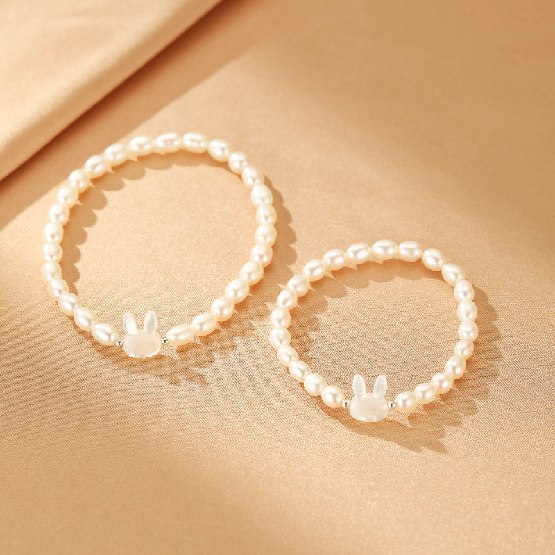 Deux bracelets en perles d'eau douce avec des breloques en forme de lapin en pierre de lune, sur un fond beige satiné.
