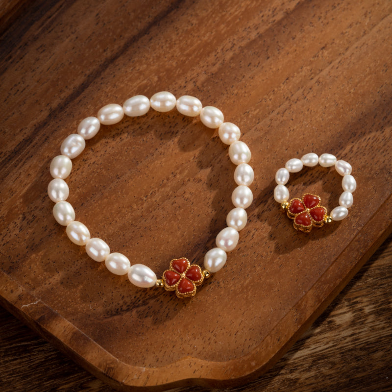 Bracelet et bague en perles d'eau douce avec un charmant trèfle en corail rouge et une monture plaquée or, présentés sur un plateau en bois.