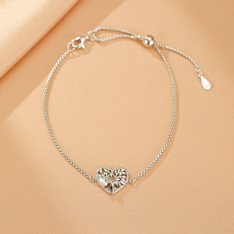Bracelet en argent avec pendentif en forme de cœur ajouré représentant l'arbre de vie, orné d'une pierre de lune irisée.