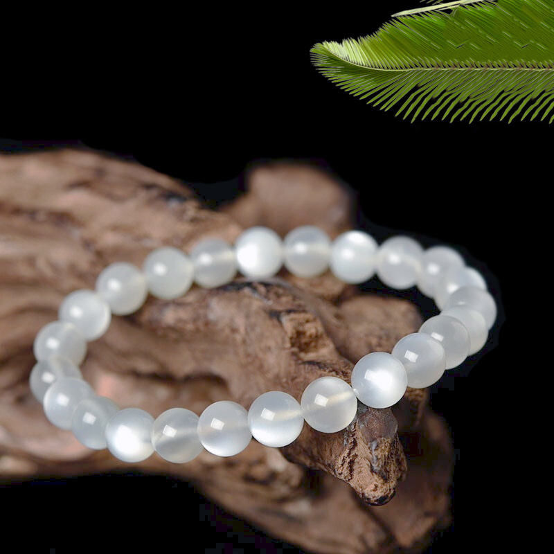 Bracelet Aura Lunaire en pierres de lune blanches sur fond noir, orné d'une branche de bois et d'une feuille de palmier.