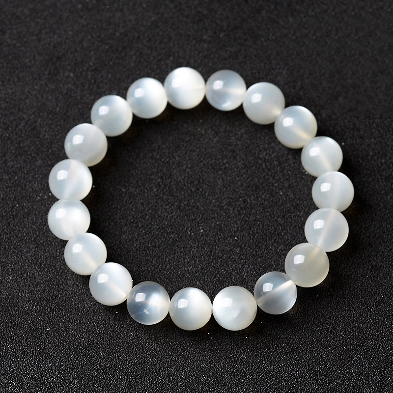 Bracelet fait de perles rondes en pierre de lune blanche naturelle, sur un fond noir.