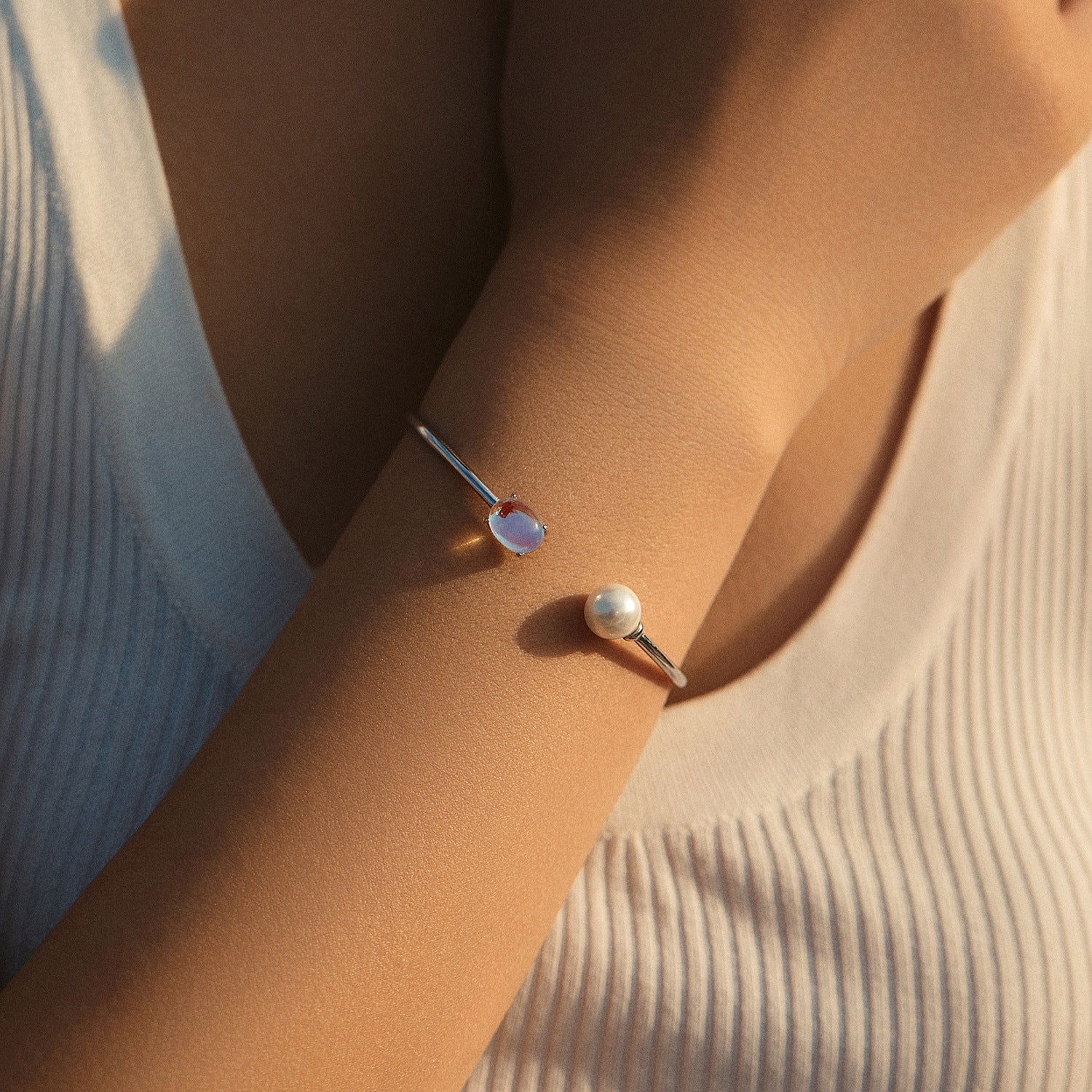 Bracelet jonc ouvert en argent 925, orné d'une pierre de lune bleutée et d'une perle blanche, porté au poignet.