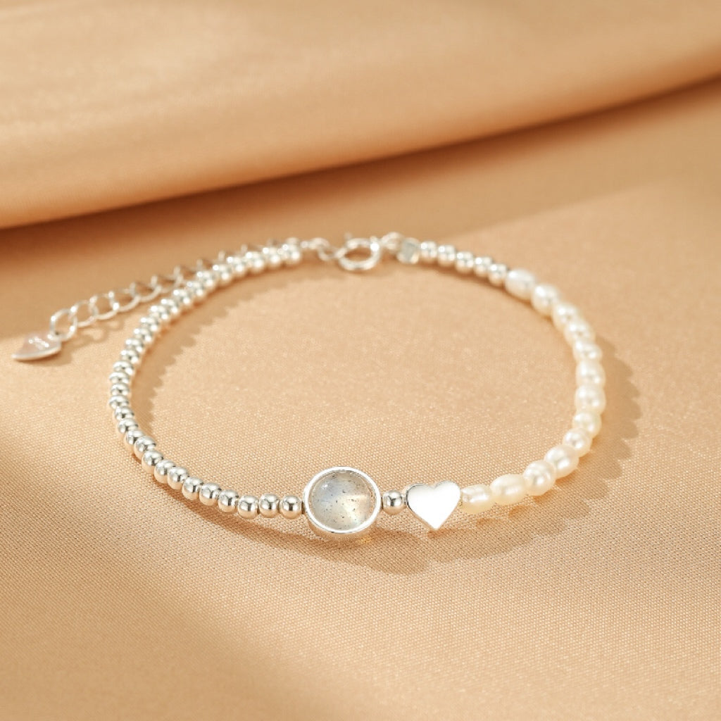 Bracelet en argent 925 avec une moitié de perles nacrées et une moitié de petites perles rondes, centré par une pierre de lune grise ronde et un petit cœur argenté.