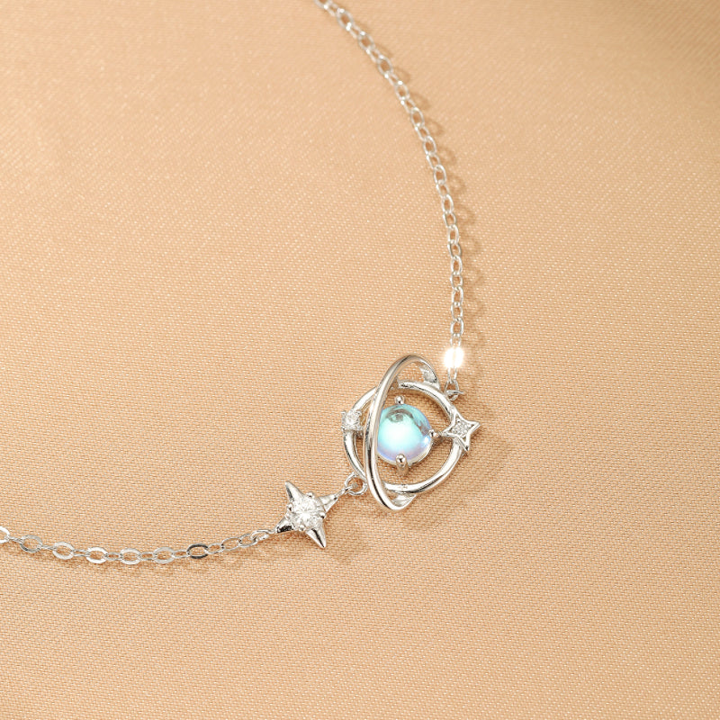 Bracelet en argent 925 avec une pierre de lune bleue opalescente au centre, entourée d'anneaux rappelant une planète et ornée d'étoiles scintillantes.