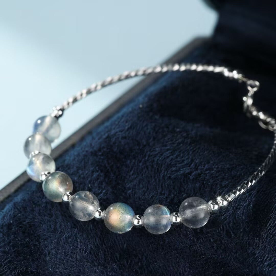 Bracelet en argent avec des perles de pierre de lune bleutées et irisées, posé sur un écrin bleu nuit.