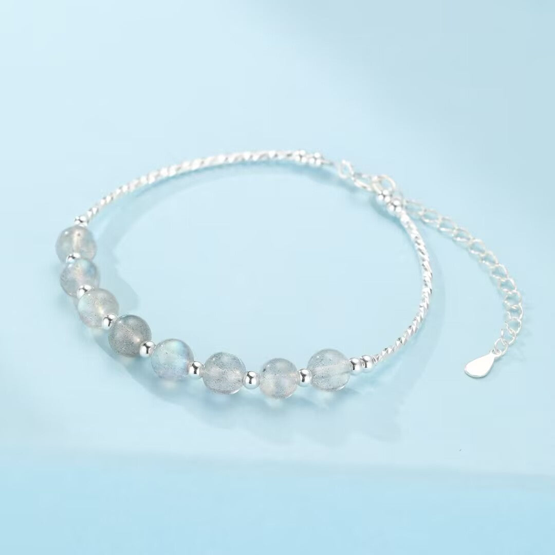 Bracelet fin en argent 925 avec des perles rondes de pierre de lune bleutée et des petites billes d'argent, fermoir ajustable.