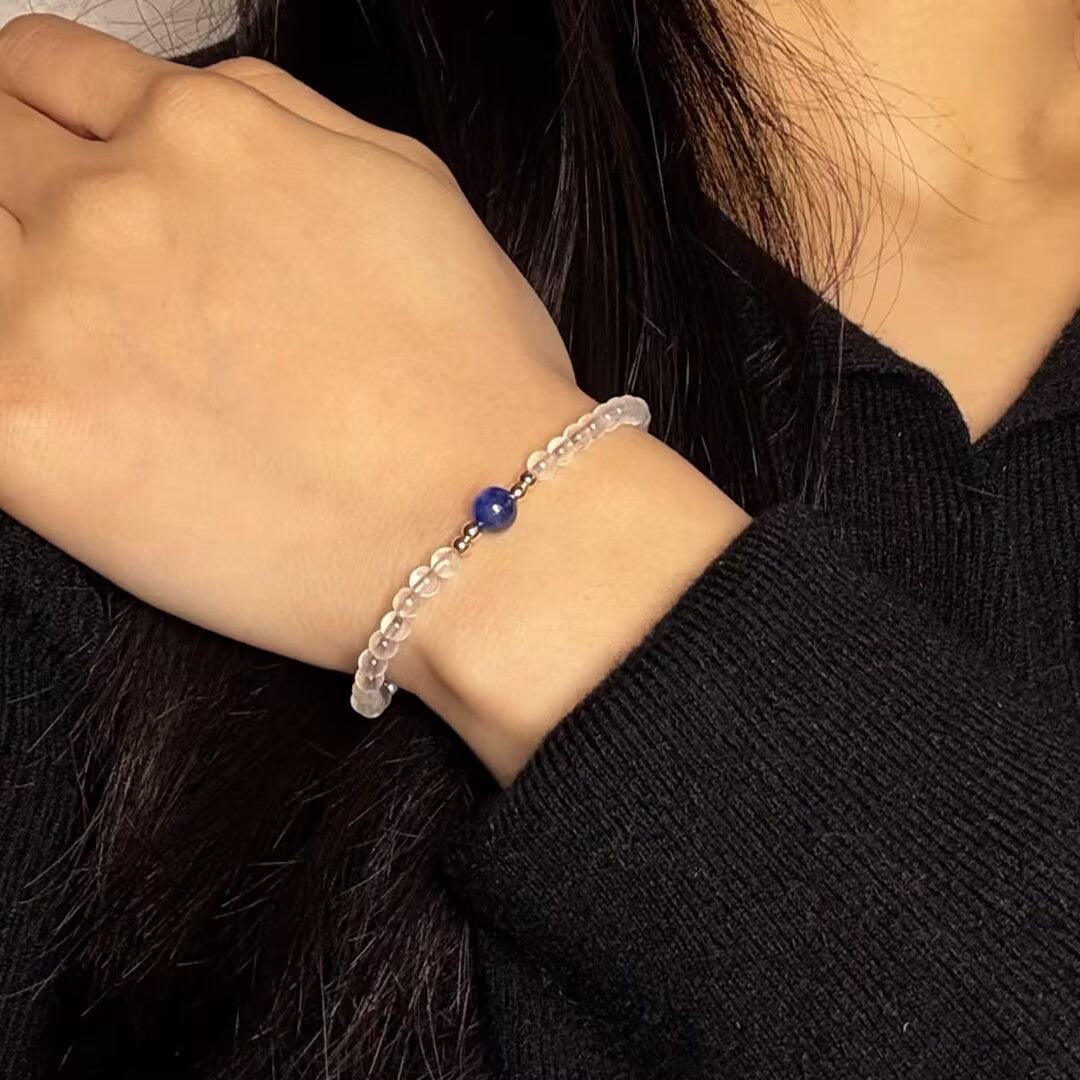 Bracelet fin avec perles transparentes et une perle bleue centrale, porté au poignet d'une femme