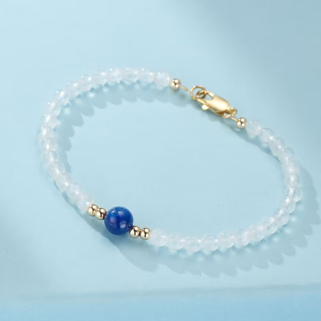 Bracelet en pierres de lune blanches et une pierre bleue centrale, avec des perles dorées et un fermoir assorti.