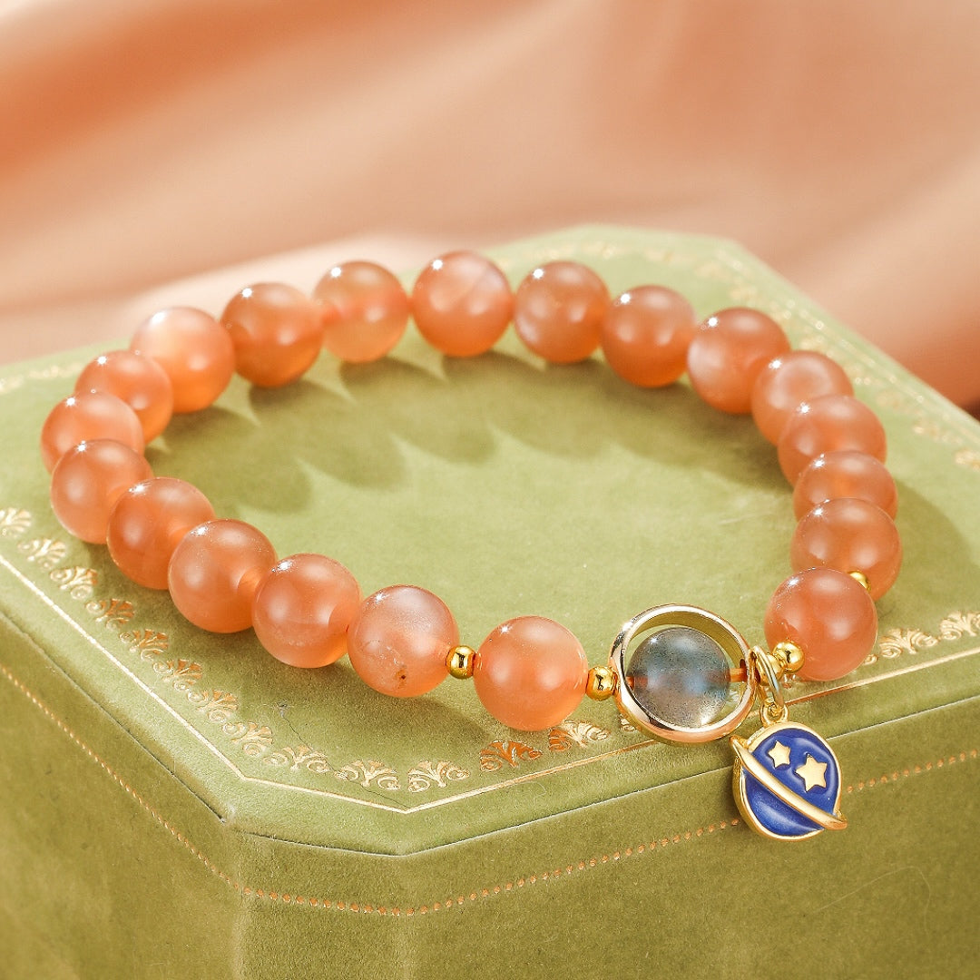 Bracelet en perles de pierre de soleil orangées avec un pendentif planète bleu et étoiles dorées, et une pierre centrale grise.