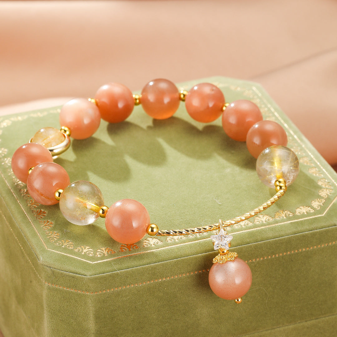 Bracelet élastique en pierre de soleil avec des perles rondes orange vif et des perles de quartz rutile, orné d'un pendentif en forme d'étoile incrusté de cristaux et d'une perle de pierre de soleil.