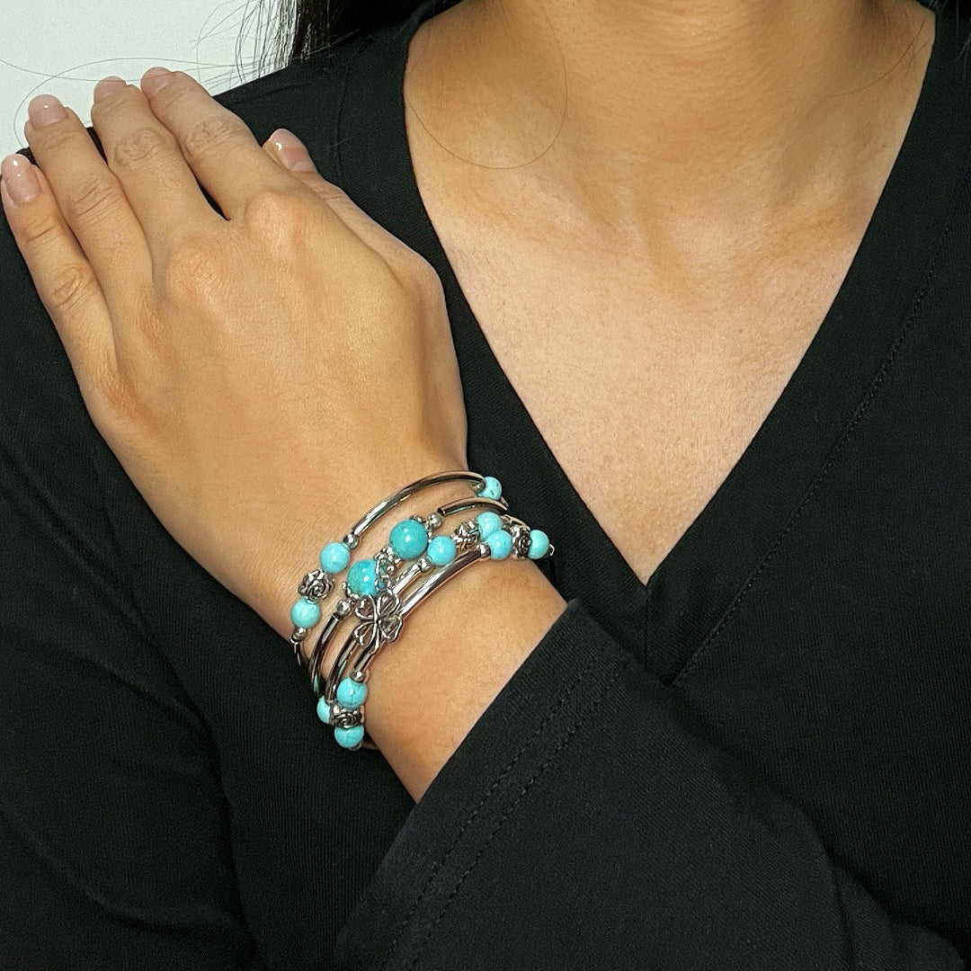 Bracelet jonc multi-rangs en argent avec perles bleu turquoise et breloque trèfle, porté au poignet d'une femme.