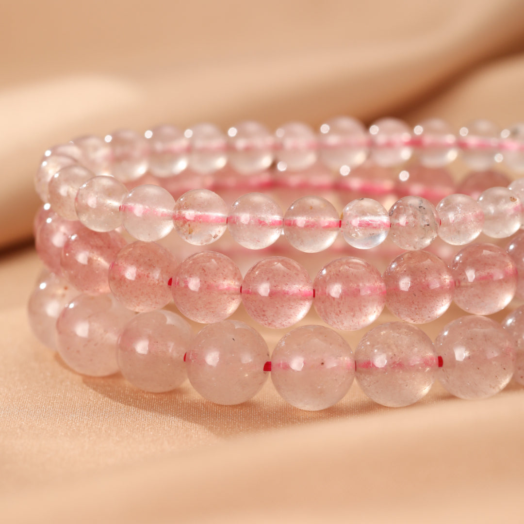 Trois bracelets en perles de quartz fraise rose translucide avec des inclusions rouges, montés sur un fil élastique.