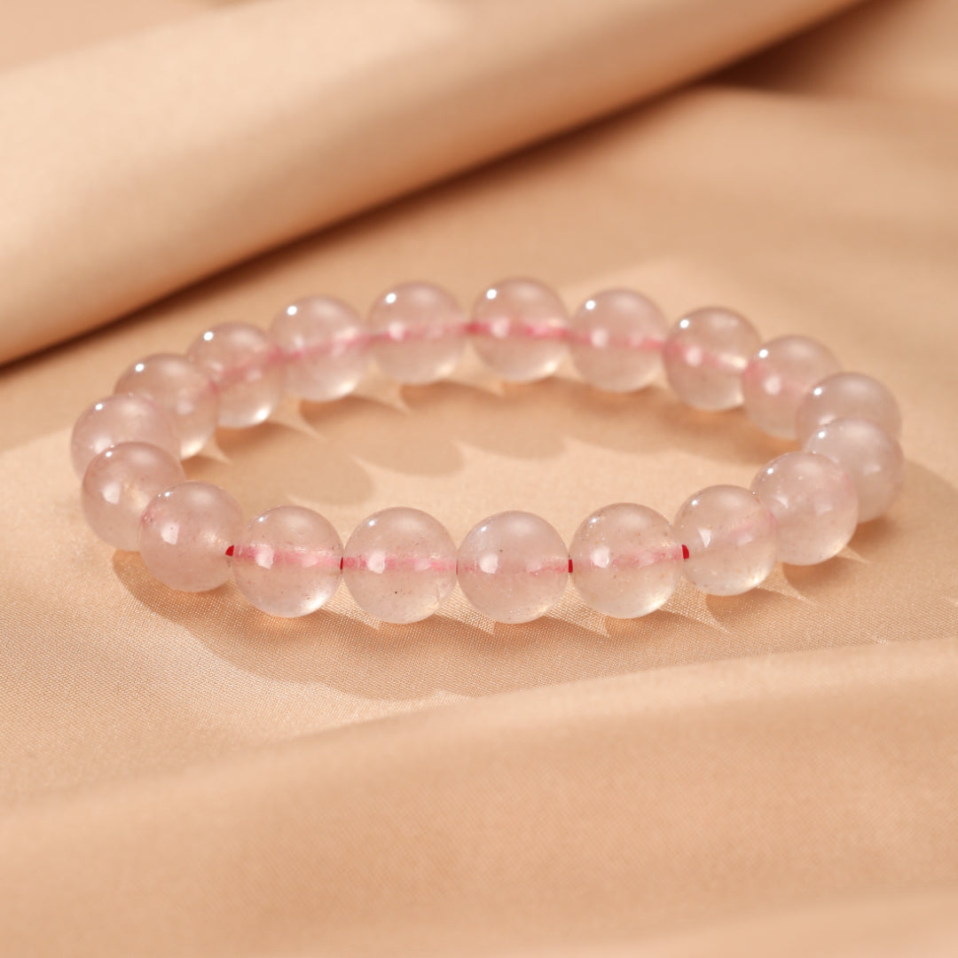 Bracelet composé de perles rondes en quartz fraise rose pâle, reliées par un fil élastique visible à travers les perles.