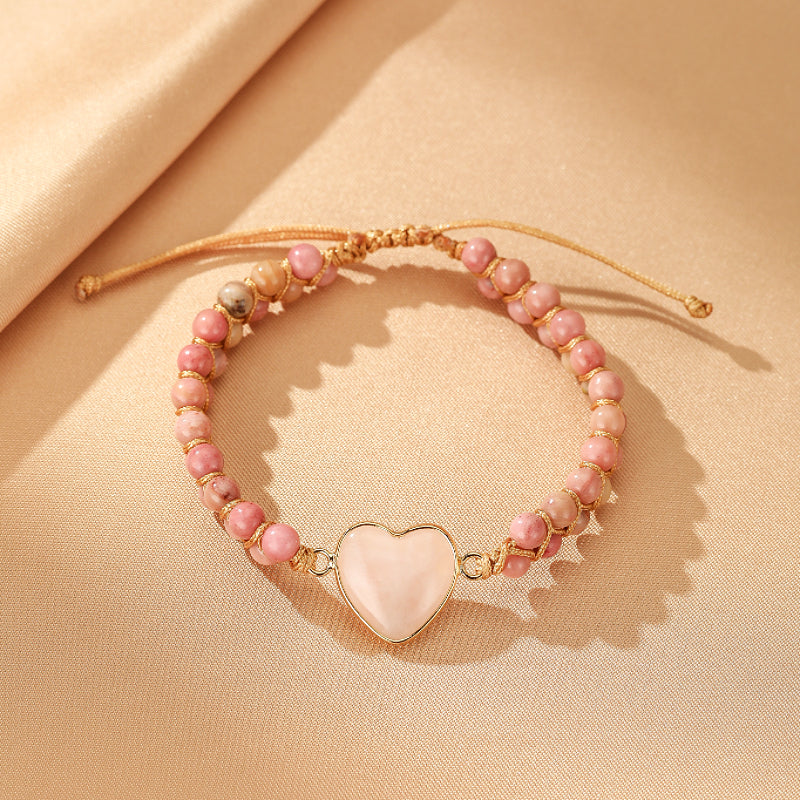 Bracelet Cœur de Joie en quartz rose, avec un pendentif en forme de cœur en pierre rose pâle, entouré de perles roses et d'un cordon doré réglable.