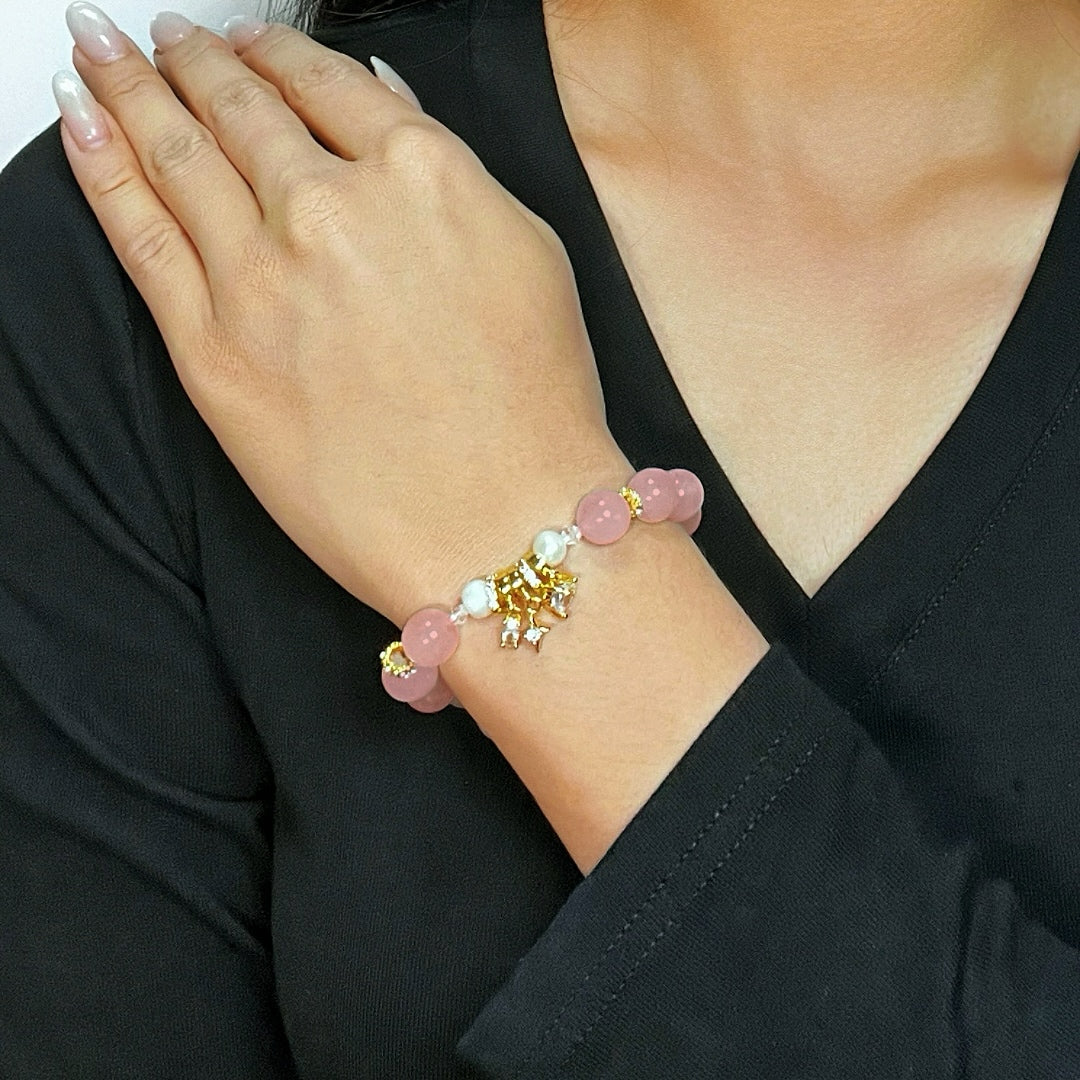 Bracelet fantaisie "Charme de Vénus" composé de perles roses en quartz, de perles blanches et d'un pendentif doré en forme de cœur orné de cristaux.
