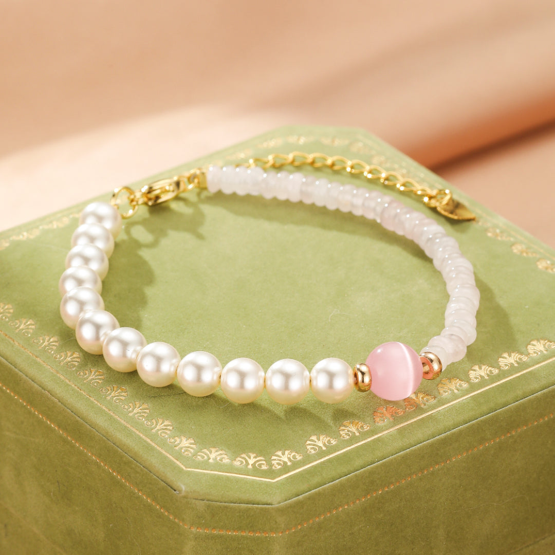 Bracelet délicat en quartz rose et perles blanches, orné d'une perle rose ronde et de détails dorés, sur un coffret vert.