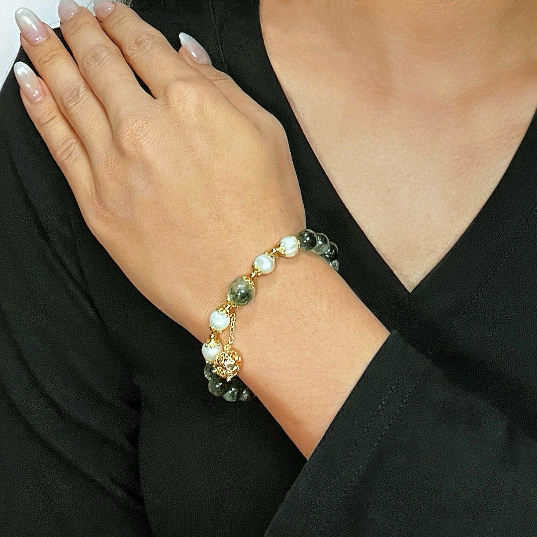 Bracelet Harmonie Royale en quartz vert et perles blanches, monté sur chaîne dorée, porté au poignet d'une femme.