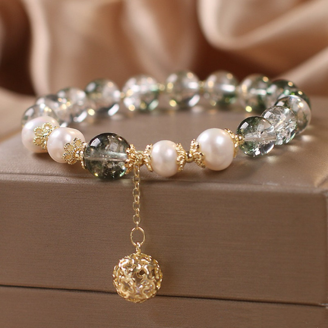 Bracelet élégant avec des perles nacrées blanches, des pierres de quartz vert transparentes et une breloque boule dorée ajourée, le tout monté sur une chaîne dorée.