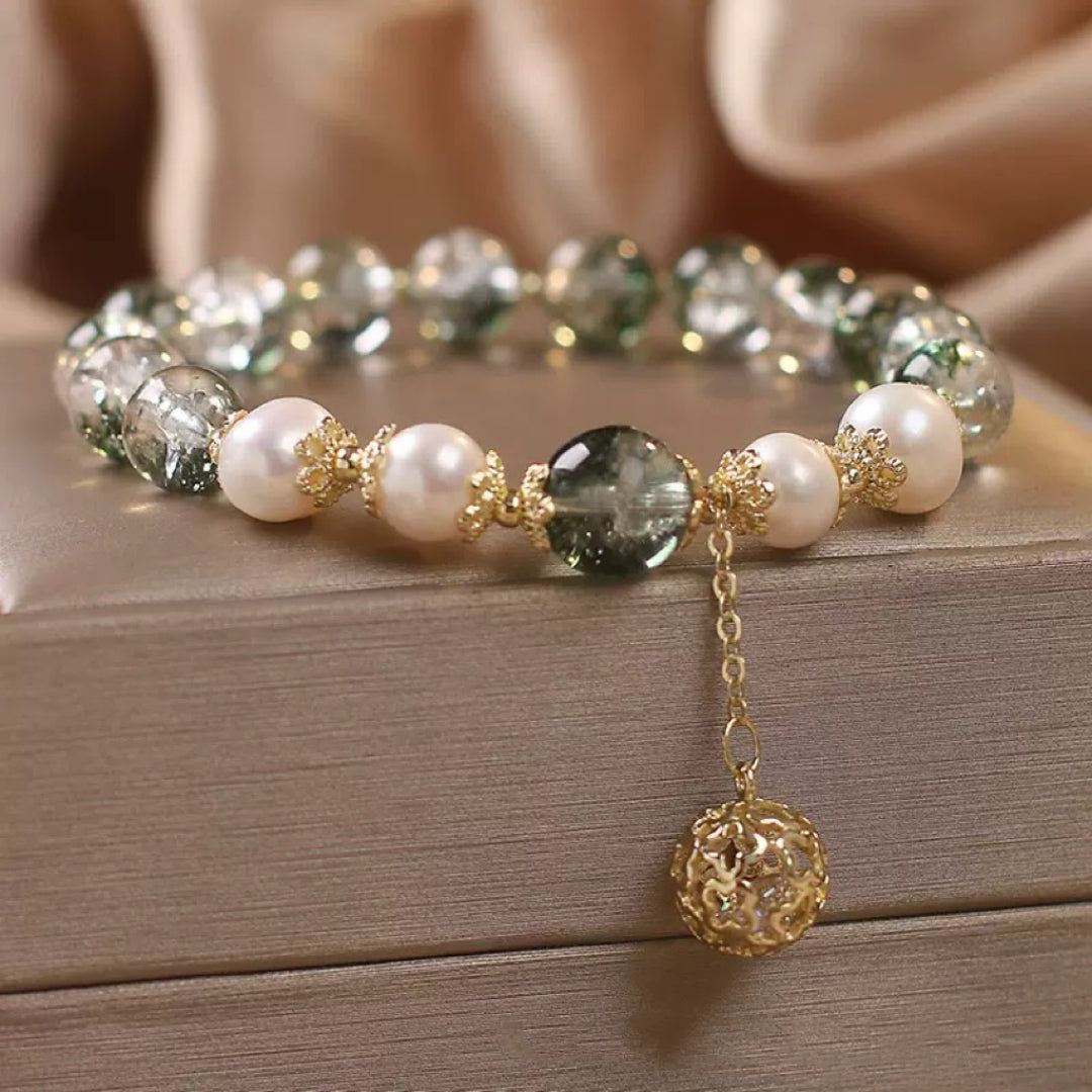 Bracelet de perles d'eau douce blanches et de quartz vert transparent, avec une breloque sphérique en or ajouré suspendue à une fine chaîne dorée.